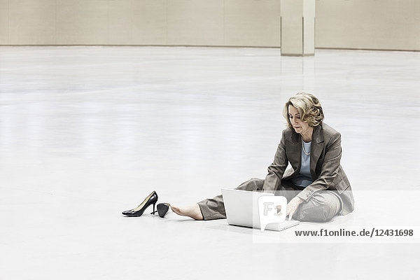 A Caucasian businesswoman working on a laptop computer while sitting on the floor of a convention centre arena.