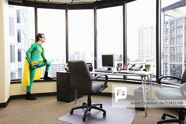 A Caucasian man office super hero stands at his office window pondering his next business move.