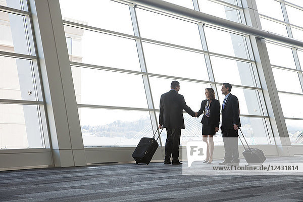 Drei Geschäftsleute treffen sich vor einem großen Fenster in der Lobby eines Kongresszentrums.