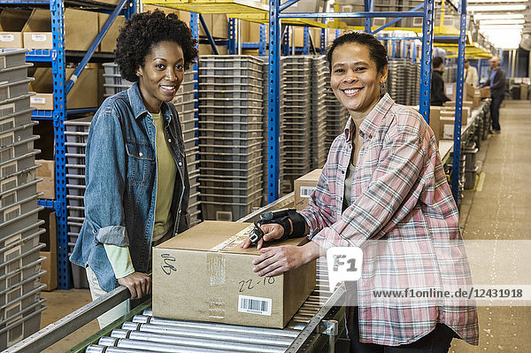 Team portrait of multi-ethnic female warehouse workers working next to a motorized feed conveyor in a large distribution warehouse.