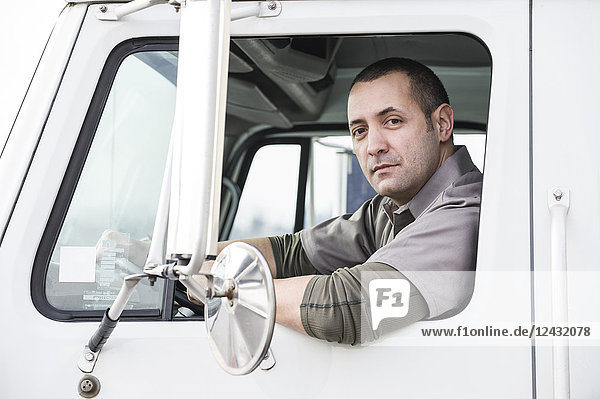 Das Porträt eines uniformierten männlichen Lkw-Fahrers im Fenster seines Lkw in einem Auslieferungslager.