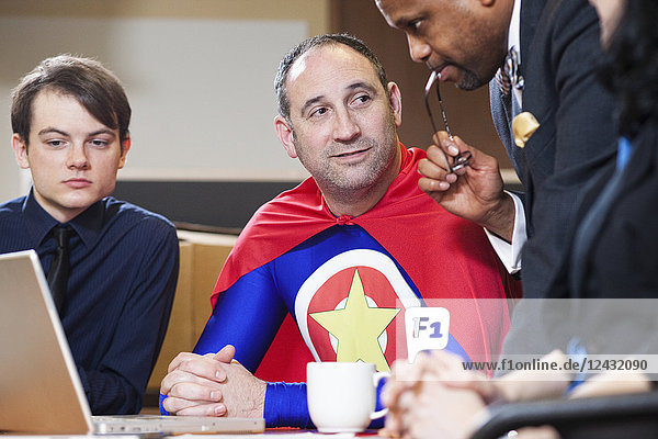 Ein kaukasischer Büro-Superheld mittleren Alters bei einem Treffen mit seinen Mitarbeitern.
