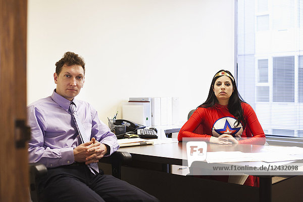 An Hispanic businesswoman office super hero and her Caucasian male team member in her office.