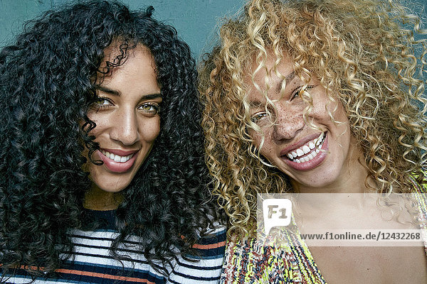 Portrait of two young women with long curly black and blond hair  smiling at camera.