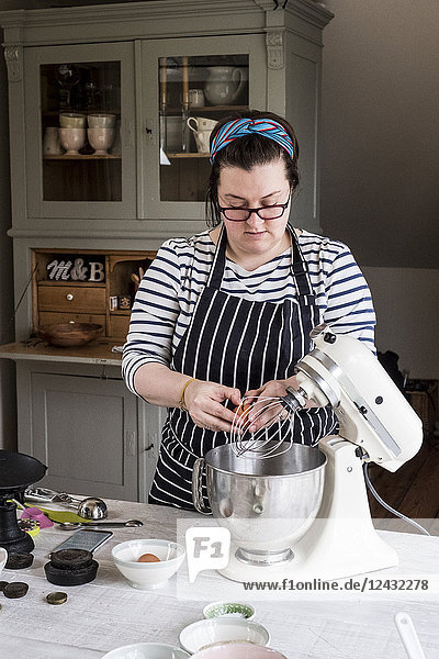 A cook in her kitchen breaking eggs and weighing ingredients for chocolate brownies.