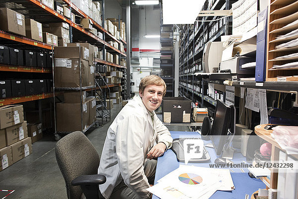 A portrait of a Caucasian male technician sitting at his desk in a parts department in a technical research and development site.