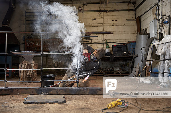Kunstschlosser bei der Arbeit in einer Werkstatt beim Löten eines Metallzauns.