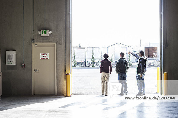 Drei Mitarbeiter warten auf eine Produktlieferung  während sie in einem Verladetor eines Auslieferungslagers stehen.