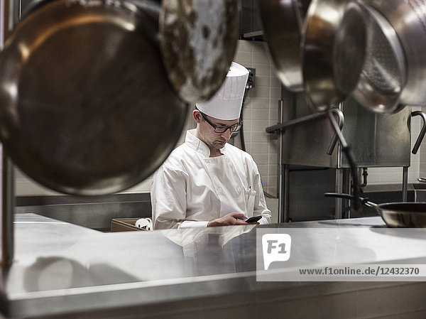 A Caucasian male chef checking his cell phone in a commercial kitchen