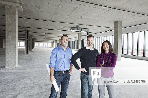 Ein Architekt und zwei Besitzer eines neuen rohen Geschäftsraums stehen in einer Reihe.