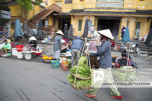 Eine Frau geht mit schweren Körben voller Gemüse über den Markt in Hoi An  Provinz Quang Nam  Vietnam  Indochina  Südostasien  Asien