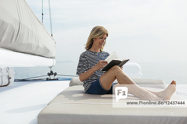 Woman sitting on deck of a catamaran  reading a book