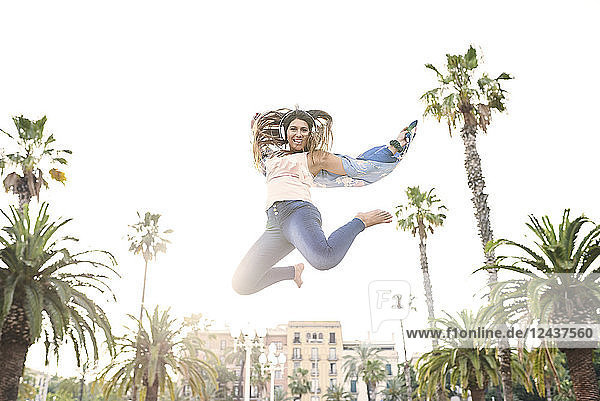 Spain  Barcelona  portrait of smiling young woman with headphones jumping in the air