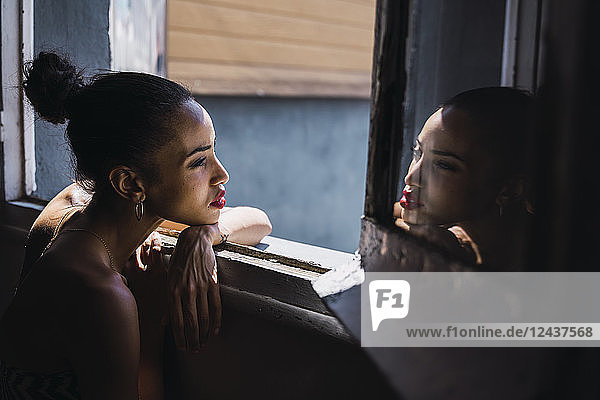 Beautiful young woman leaning on window frame reflected in mirror