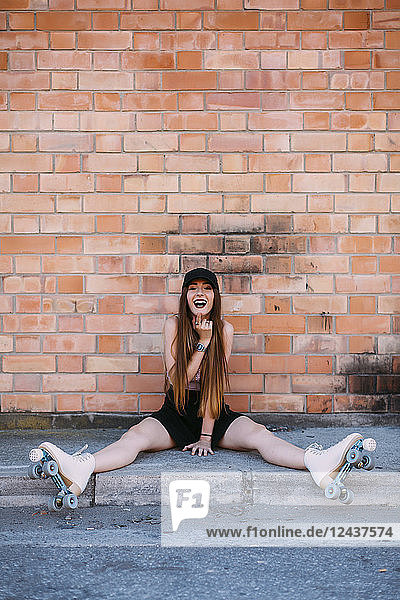 Portrait of laughing young woman with roller skates sitting on sidewalk