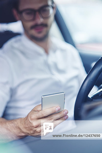 Hand of businessman sitting in car holding cell phone