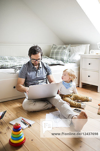 Father at home with his little son using laptop