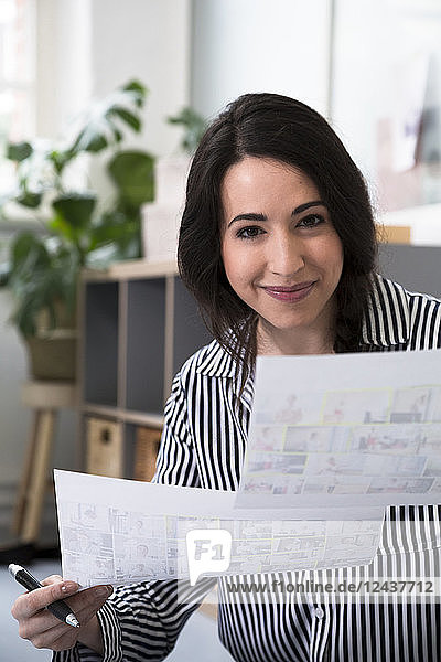 Portrait of smiling woman holding sheets of paper in office