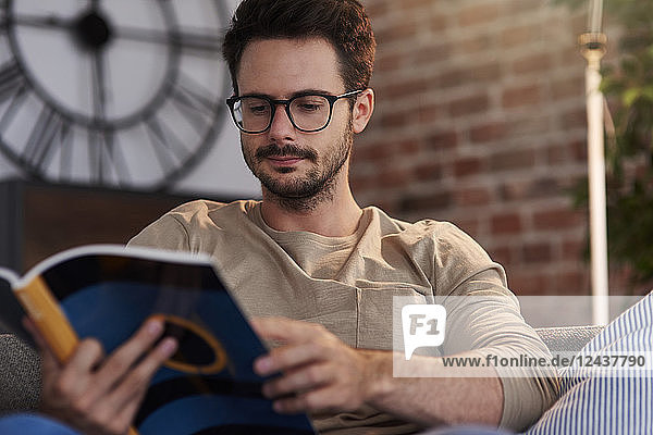 Portrait of man sitting on couch at home reading a book