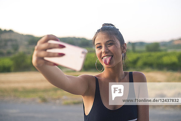Portrait of teenage girl taking selfie with smartphone while sticking out tongue