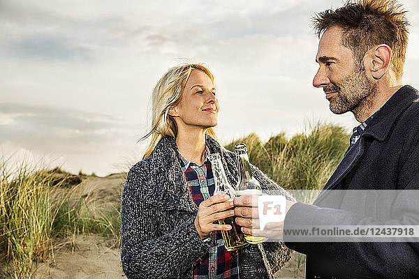 Smiling couple in dunes clinking beer bottles