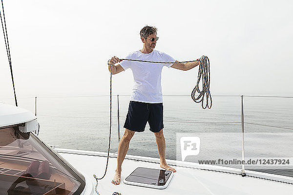 Mature man standing on catamaran  coiling rope