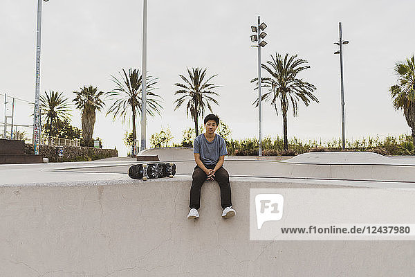 Young Chinese man sitting on wall of a skate park near the beach