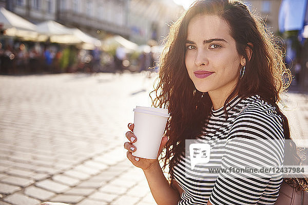 Portrait of beautiful young woman with takeaway coffee in the city