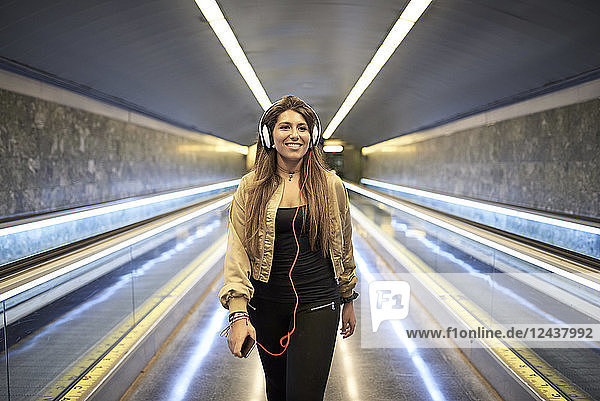 Portrait of smiling woman with headphones and smartphone in underground station