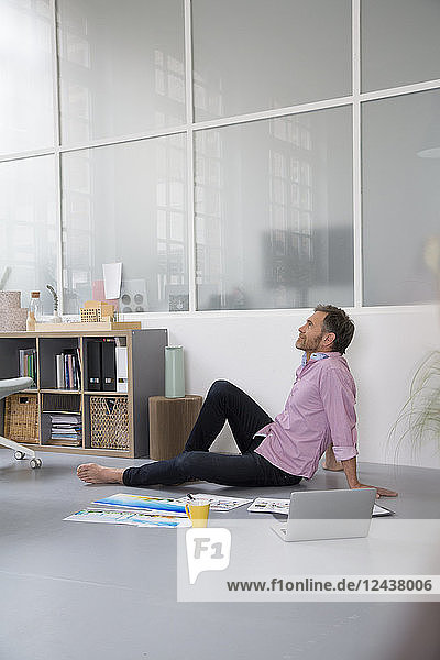 Casual man with plans and laptop sitting on the floor in a loft office