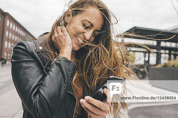 Happy young woman with windswept hair using cell phone in the city