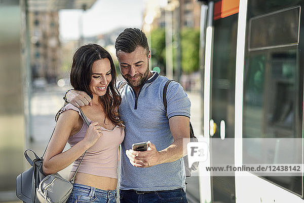 Couple looking at smartphone while waiting for tram at the station