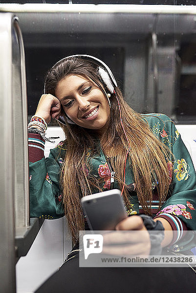 Portrait of smiling woman with headphones looking at cell phone in underground train