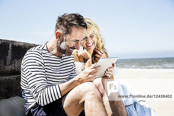 Happy couple on the beach looking at tablet