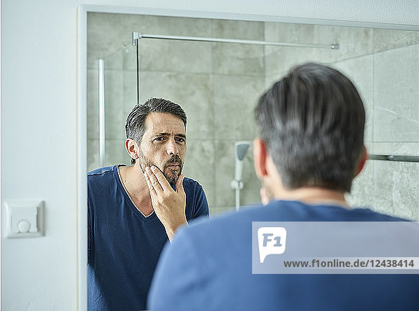 Serious man looking in bathroom mirror