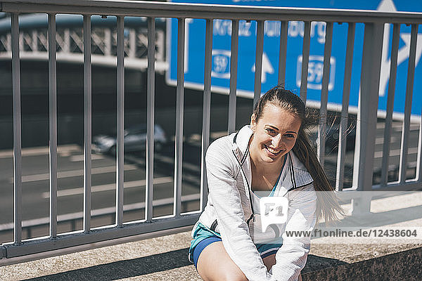 Smiling sportive young woman sitting at motorway