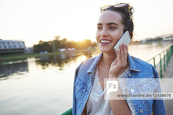 Smiling young woman on cell phone at the riverside at sunset