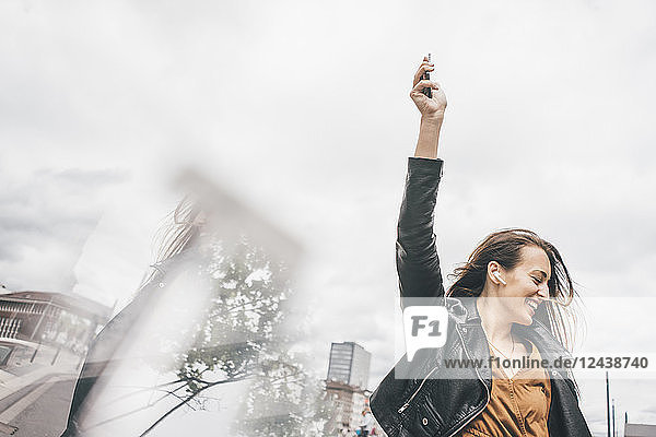 Happy young woman with in-ear phones and cell phone