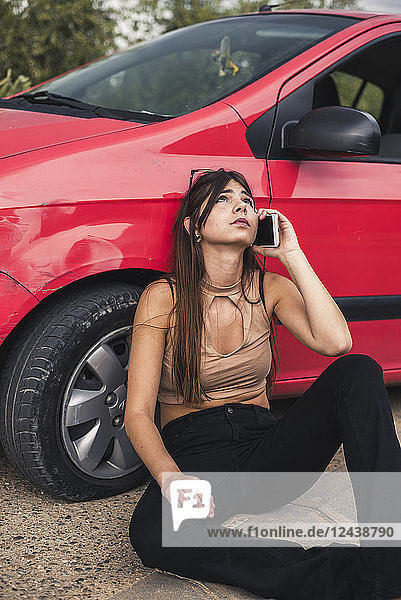 Young woman sitting at roadside having a car breakdown calling breakdown service