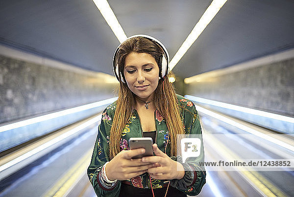 Portrait of woman with headphones looking at cell phone in underground station
