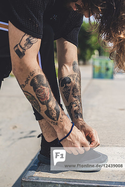 Man with tattooed arms tying his shoes  partial view