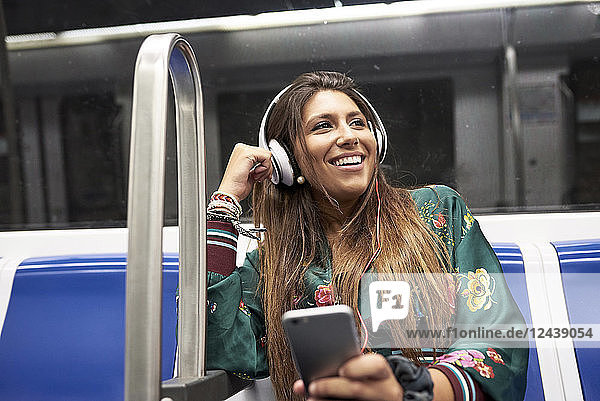 Portrait of happy woman listening music with headphones and smartphone in underground train