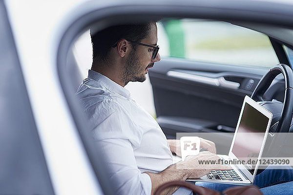 Businessman sitting in car working on laptop