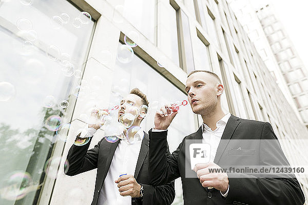Two young businessmen blowing soap bubbles outdoors