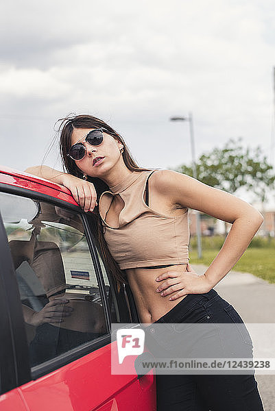 Portrait of young woman wearing sunglasses leaning on car