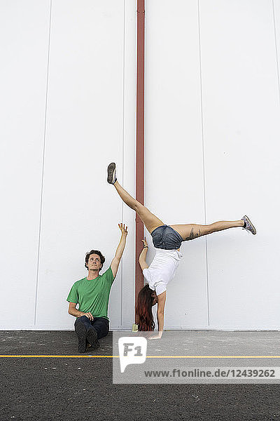 Man spotting woman  doing a one-armed handstand