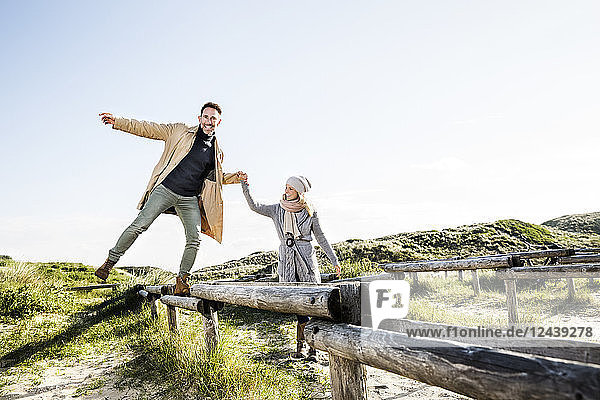 Woman helping man balancing on wooden stakes in dunes