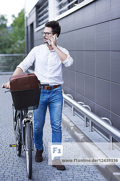 Businessman on the phone pushing his bicycle