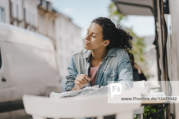 Young woman sitting in front of coffee shop with eyes closed  enjoying the sun