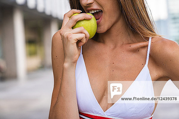 Close-up of young woman wearing sports bra eating an apple